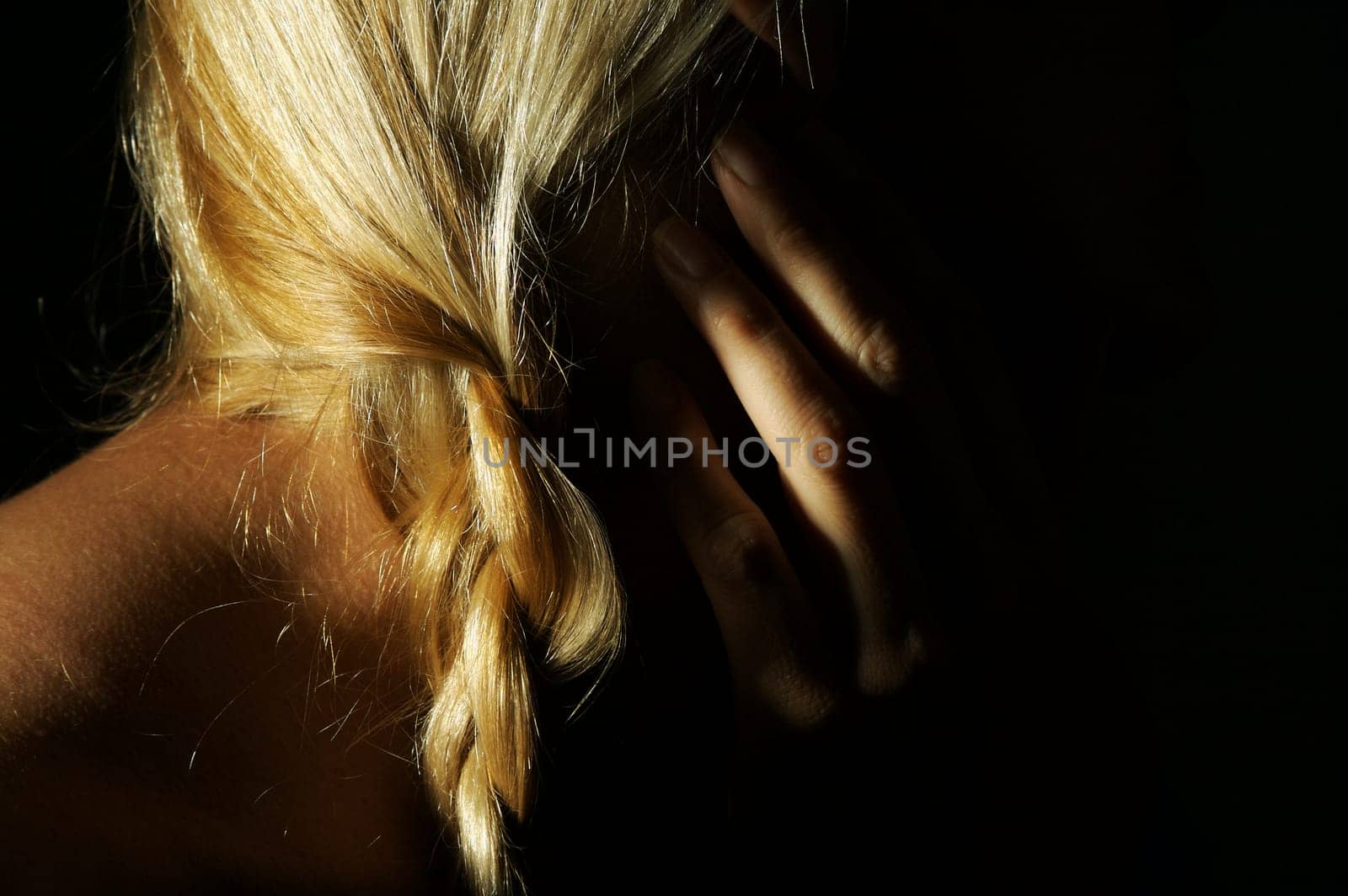 Abstract dramatically lit image of woman's shoulder, hand and blond hair on a black background.