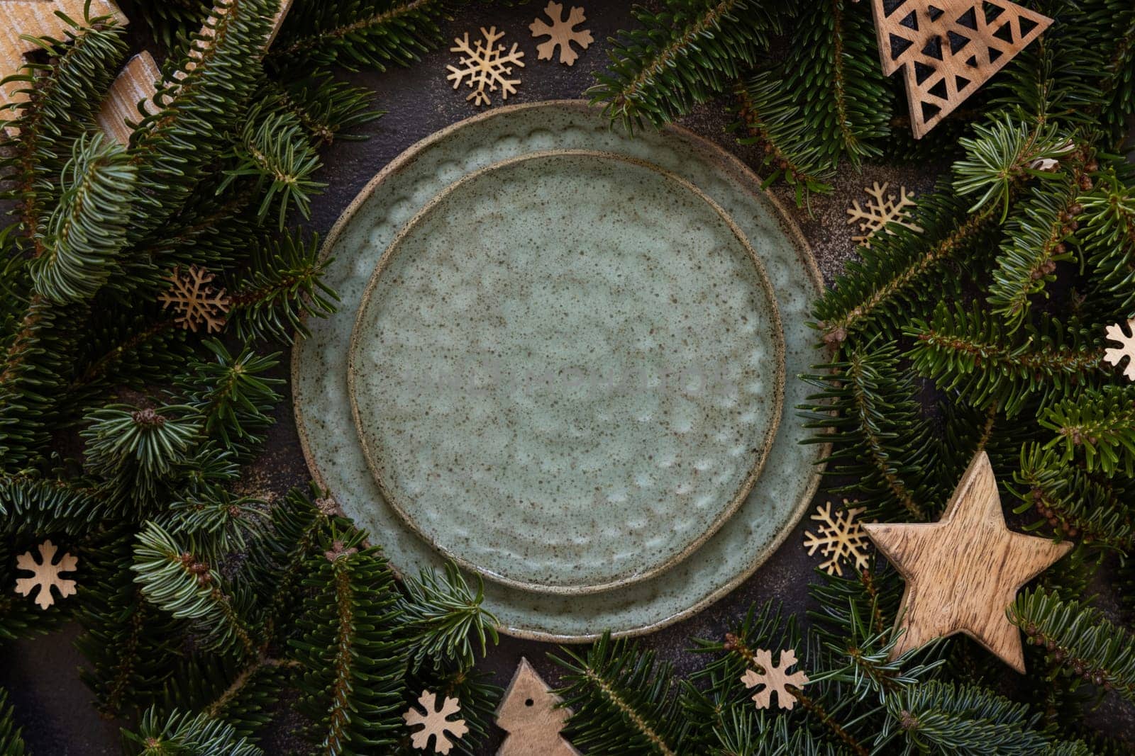 Festive table setting near fir tree branches and Rustic wooden decorations top view, copy space,. Christmas or New Year table place with green plates on dark table flat lay. Winter season, restaurant catering