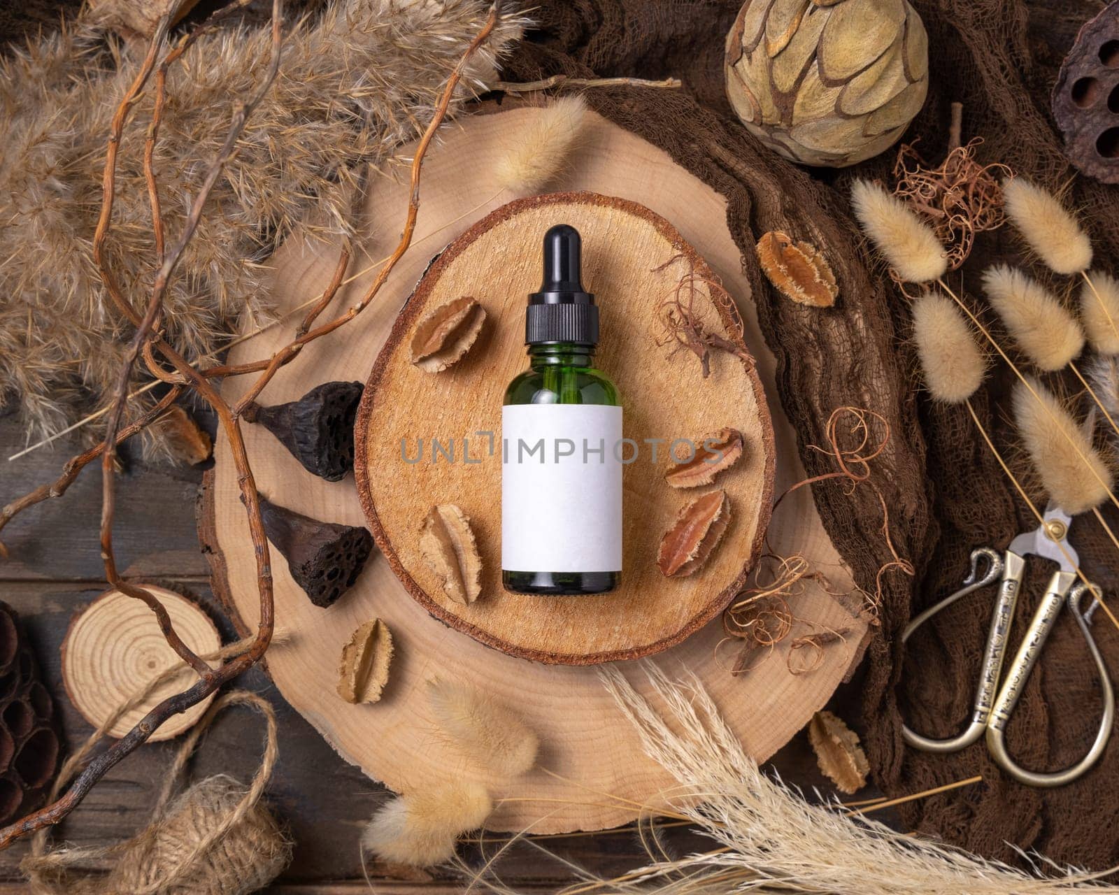 Green glass dropper bottle on wood near natural boho decorations top view, cosmetic packaging mockup. Skincare beauty product, serum or essence. Bohemian eco friendly flat lay with dried leaves.