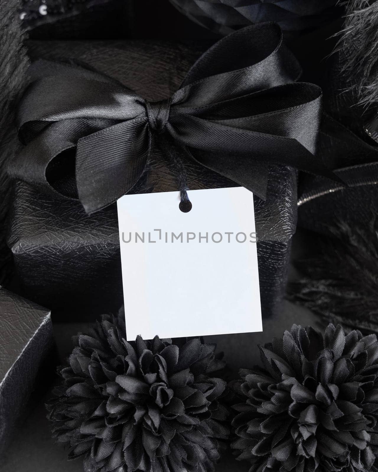 Wrapped Gift Boxes with black paper flowers and decorations and square gift tag, mockup, copy space. Dark composition with blank label card for Birthday, Anniversary or black party present
