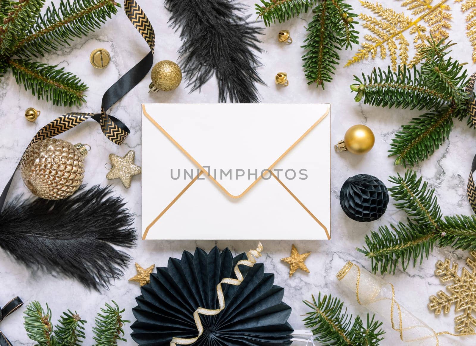 Paper envelope between black and golden Christmas decorations and fir tree branches top view. Winter composition with blank invitation card Mockup, copy space