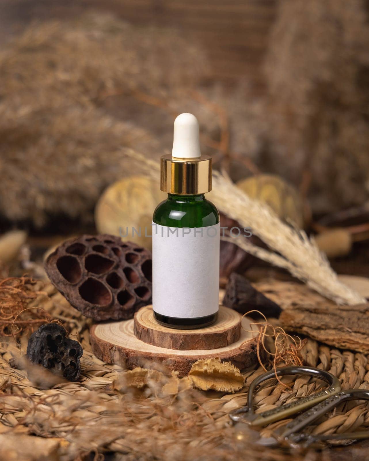 Green glass dropper bottle on wood near natural boho decorations close up, cosmetics label mockup. Eco friendly Skincare beauty product, serum or essence. Bohemian composition with dried leaves and flowers.