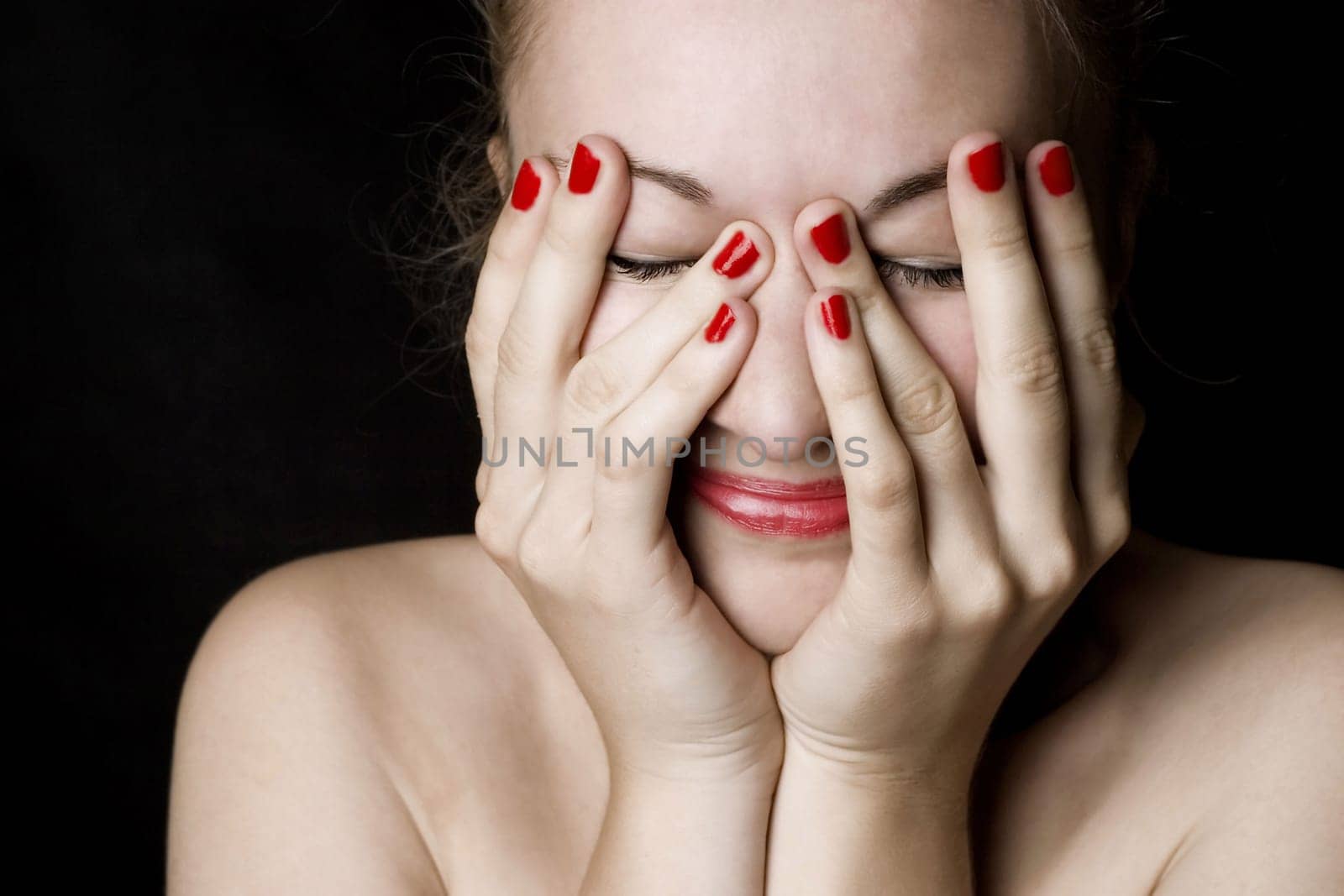 Beautiful smiling young woman with red lips and nails. Black background.