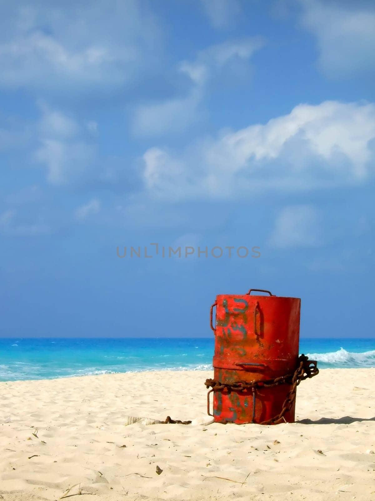 A red barrel with a chain around it standing still on the beach.