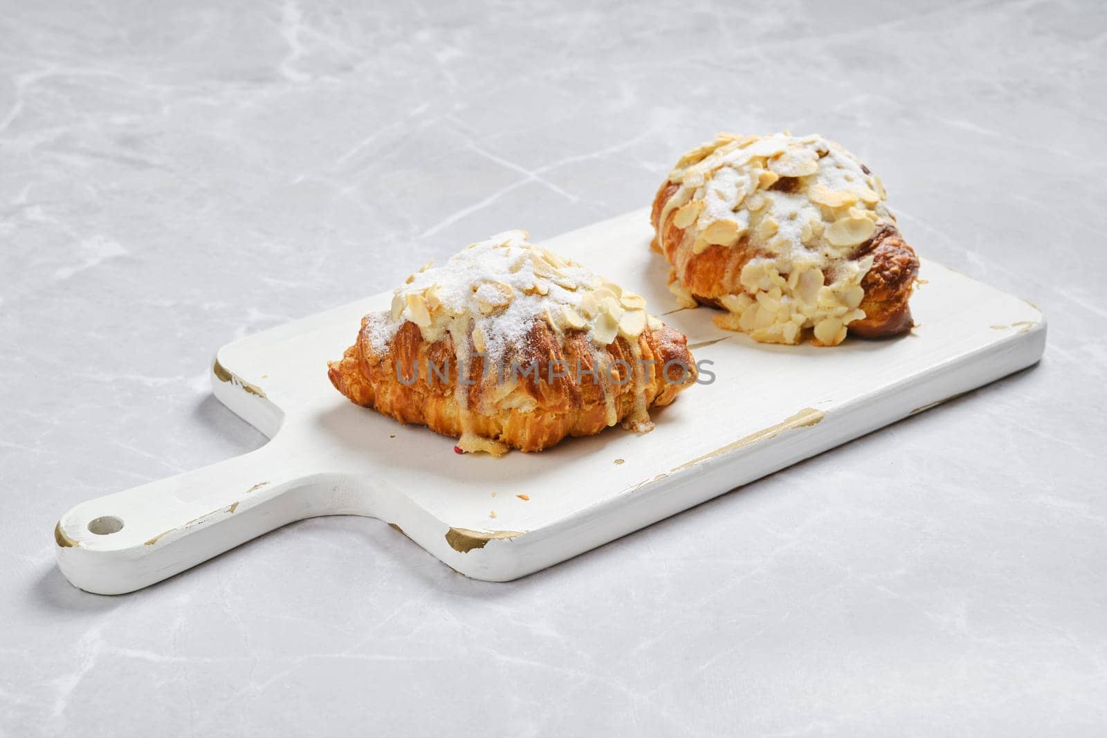 Crispy croissant with caramel and peanut shavings on white serving board on marble surface