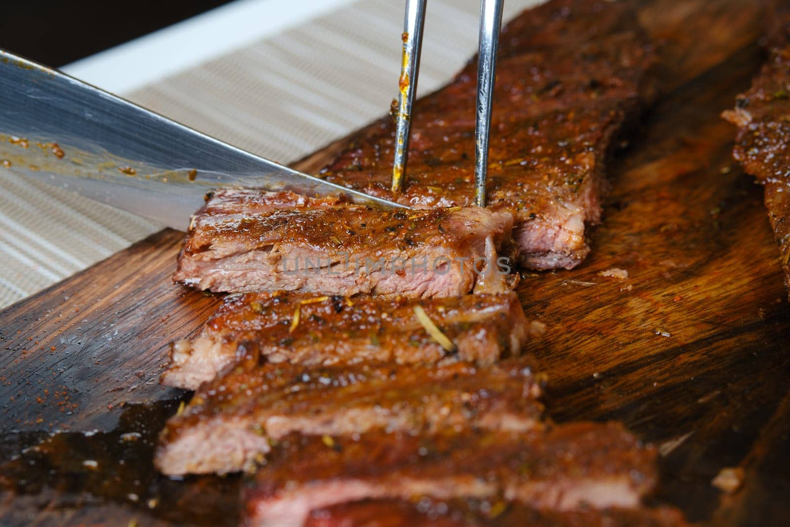 Cutting juicy grilled top blade beefsteak on wooden cutting board (photo with shallow depth of field)