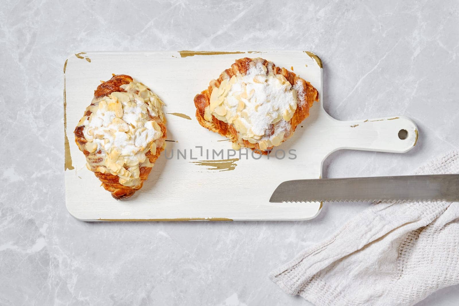 Top view of crispy croissant with caramel and peanut shavings on white serving board on marble background
