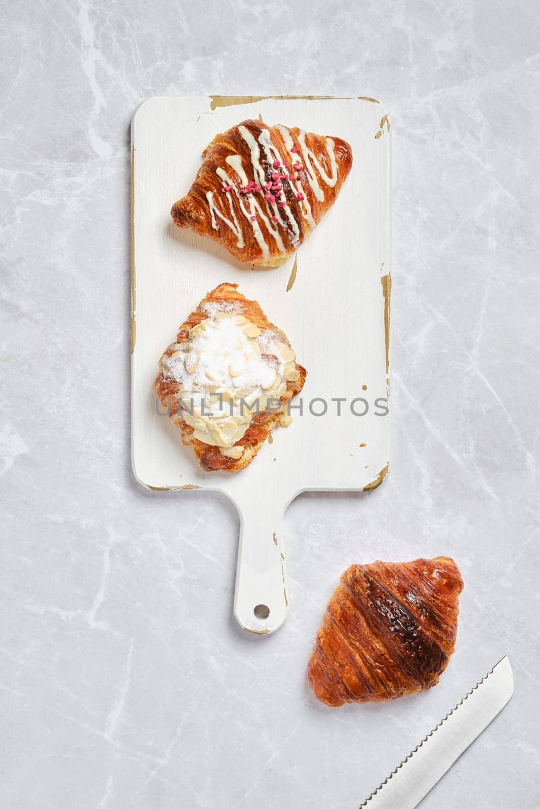 Top view of assortment of fresh croissants on white serving board on marble background