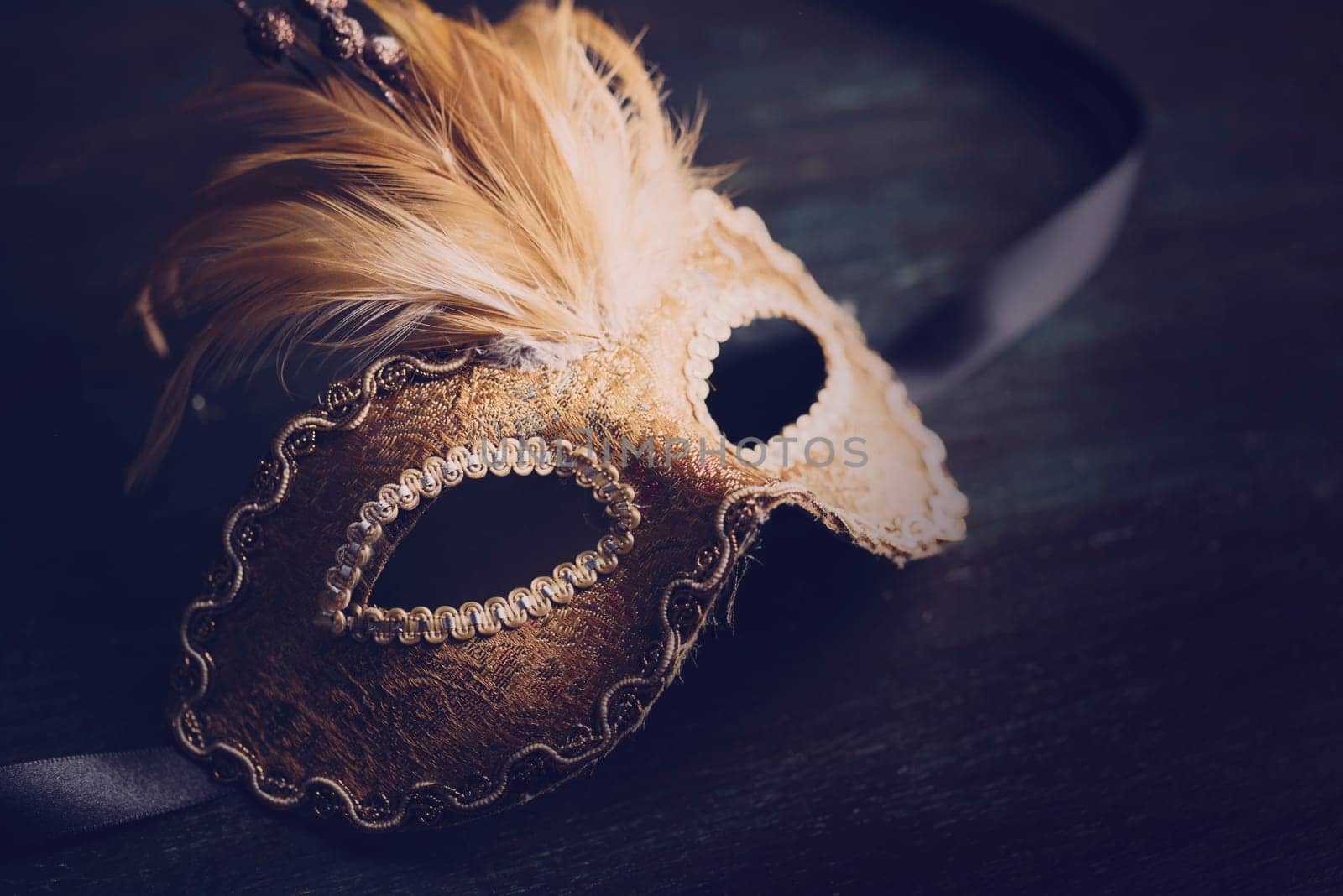 Golden venetian ball mask over dark background with copyspace. Masquerade party or holiday event celebration concept.