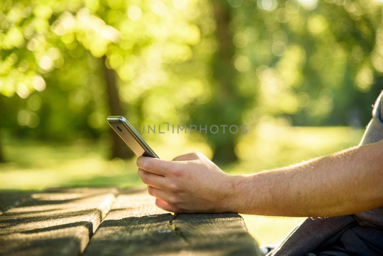 Man relaxing in park and using mobile smart phone for social media leisure. Closeup on hand holding cell phone and texting. Green nature environmet bokeh background. Wireless technology and internet business concept.