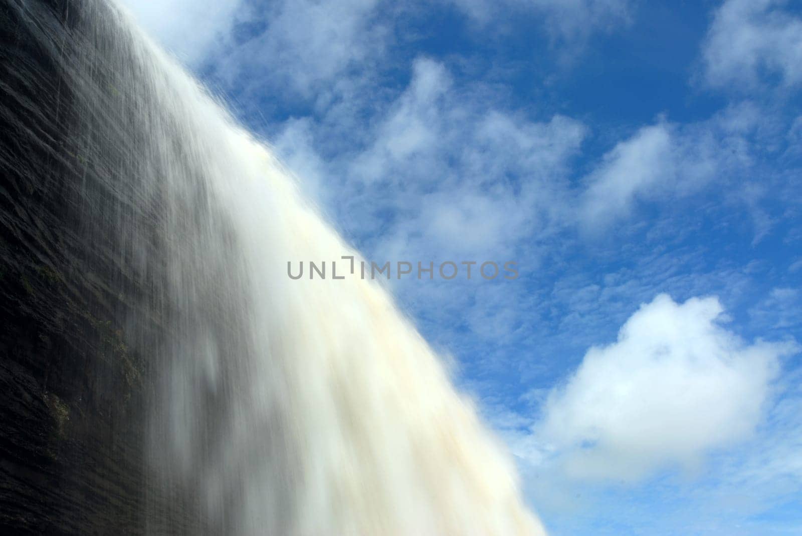 Water falls over a cliff surrounded by a blue sky with clouds.
