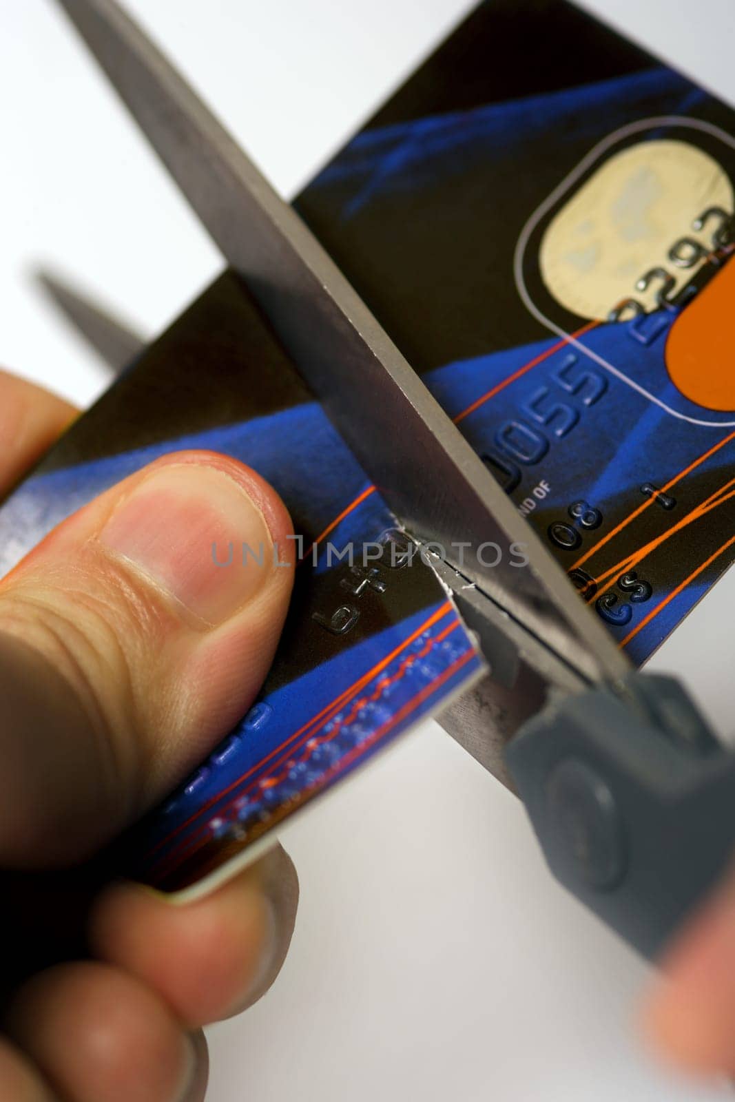 Macro image of scissors cutting through a credit card.  Logos are fake and numbers have been changed.  Colours of the card have been altered also.