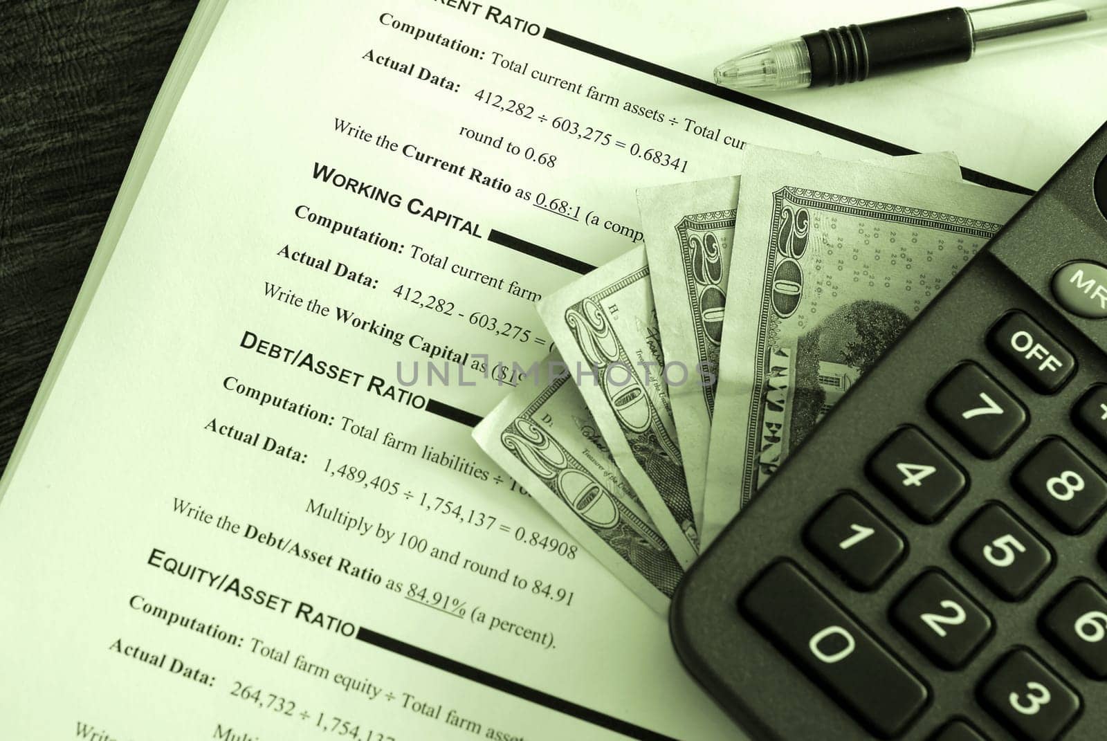 Calculator, pen and money on top of a business financial worksheet-image done with a green tint
