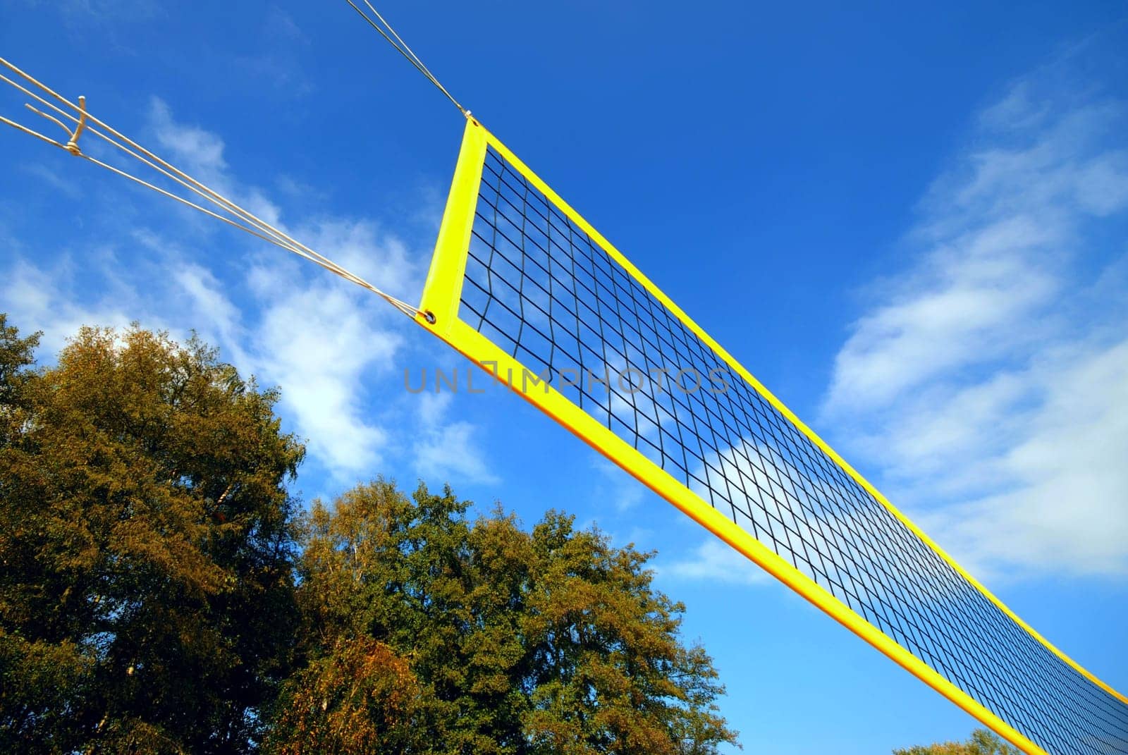 yellow volleyball net under blue clouded sky, in the background autumn trees