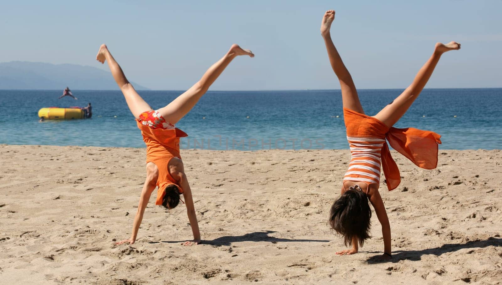 Two girls in orange clothes doing cartwheel on the beach