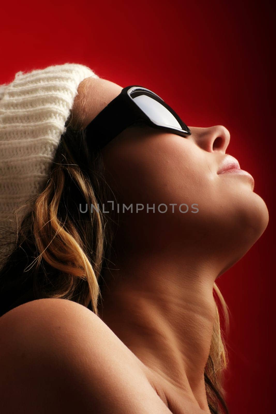 portrait of a beautiful woman with a cap and some sunglasses against red background
