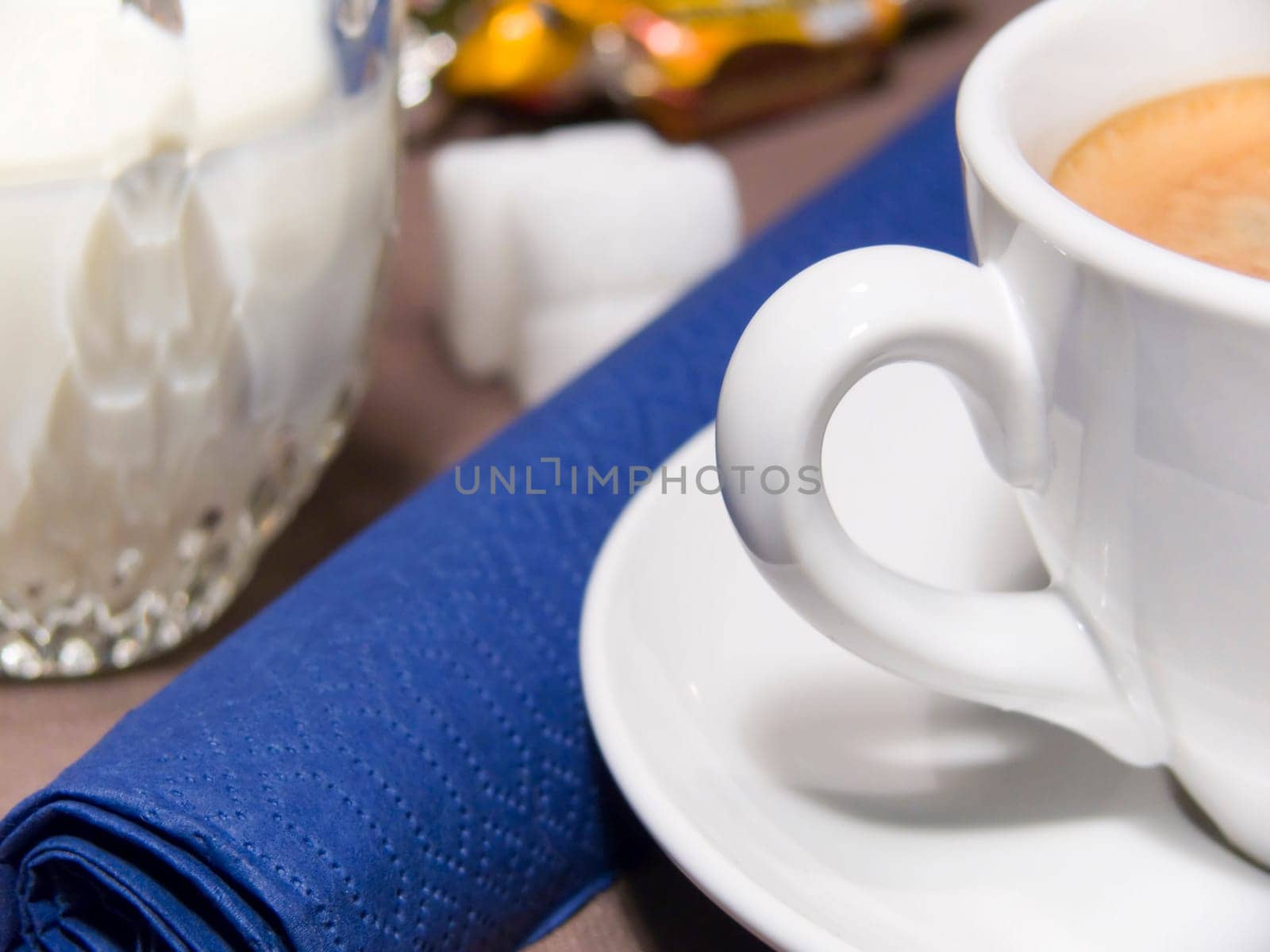 A cup of coffee with foam, milk, sugar and a blue napkin
