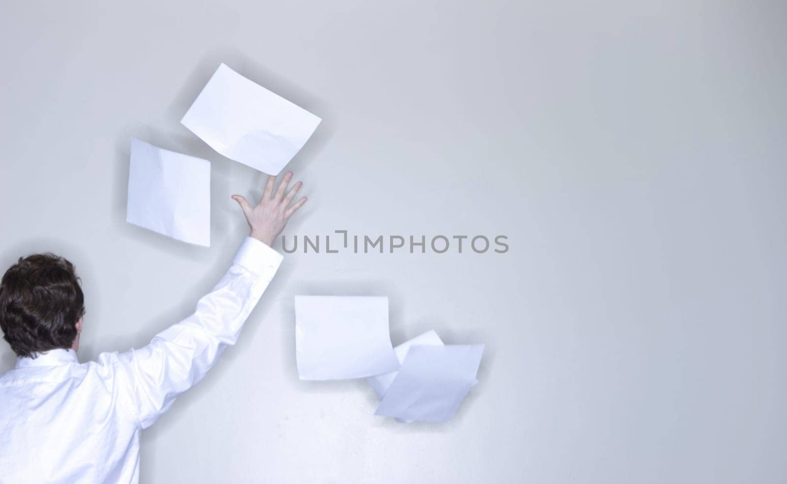 rear view of single man in white shirt raising his arm releasing stack of paper