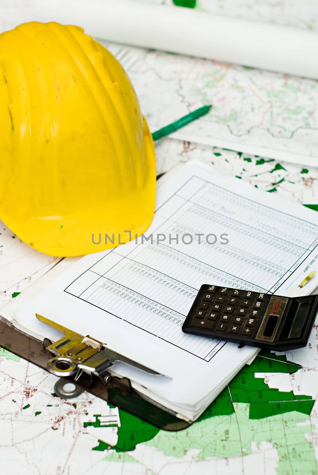 yellow hart hat, clipboard and calculator lying on maps and different plans