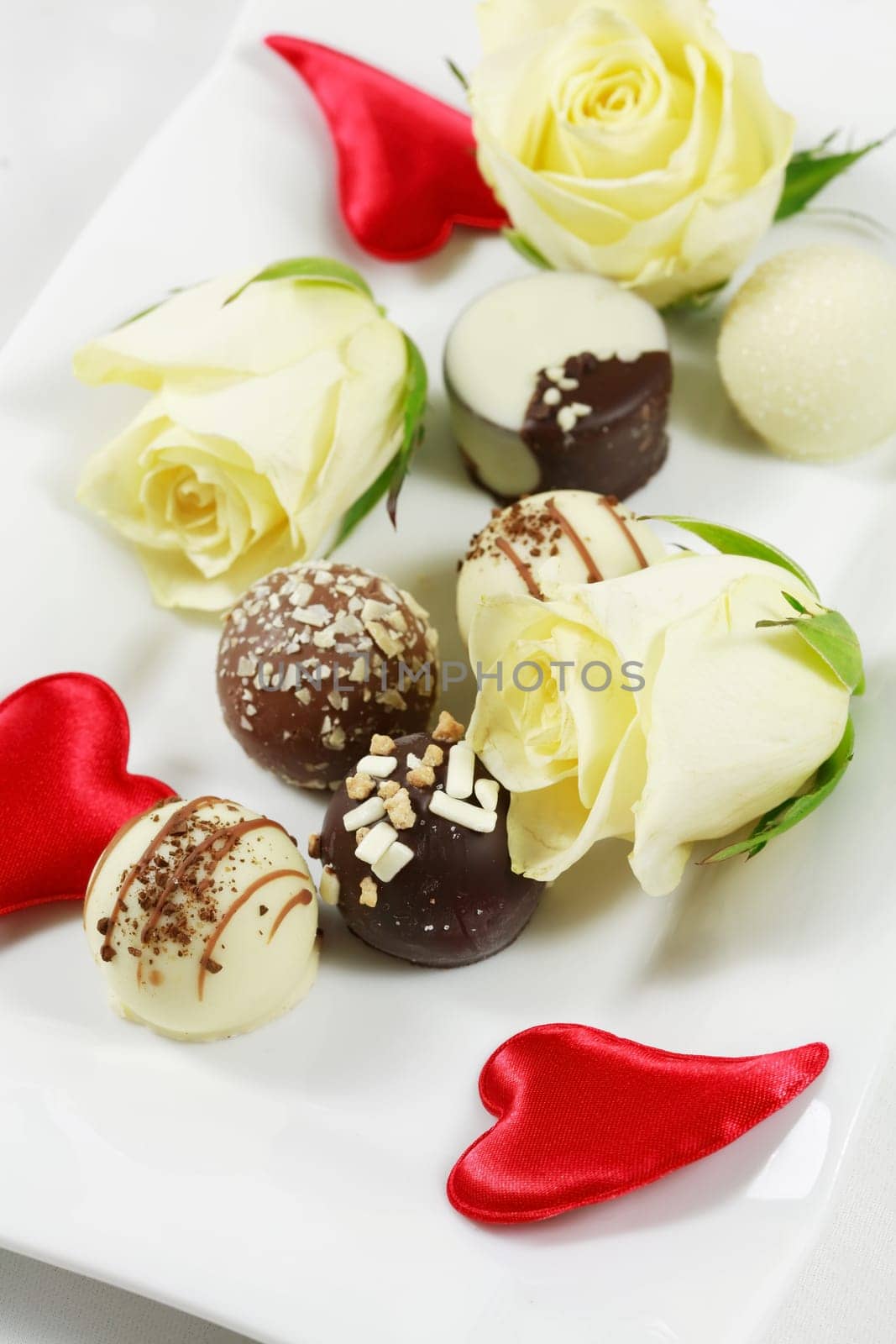 Delicious chocolate pralines with rose on white plate