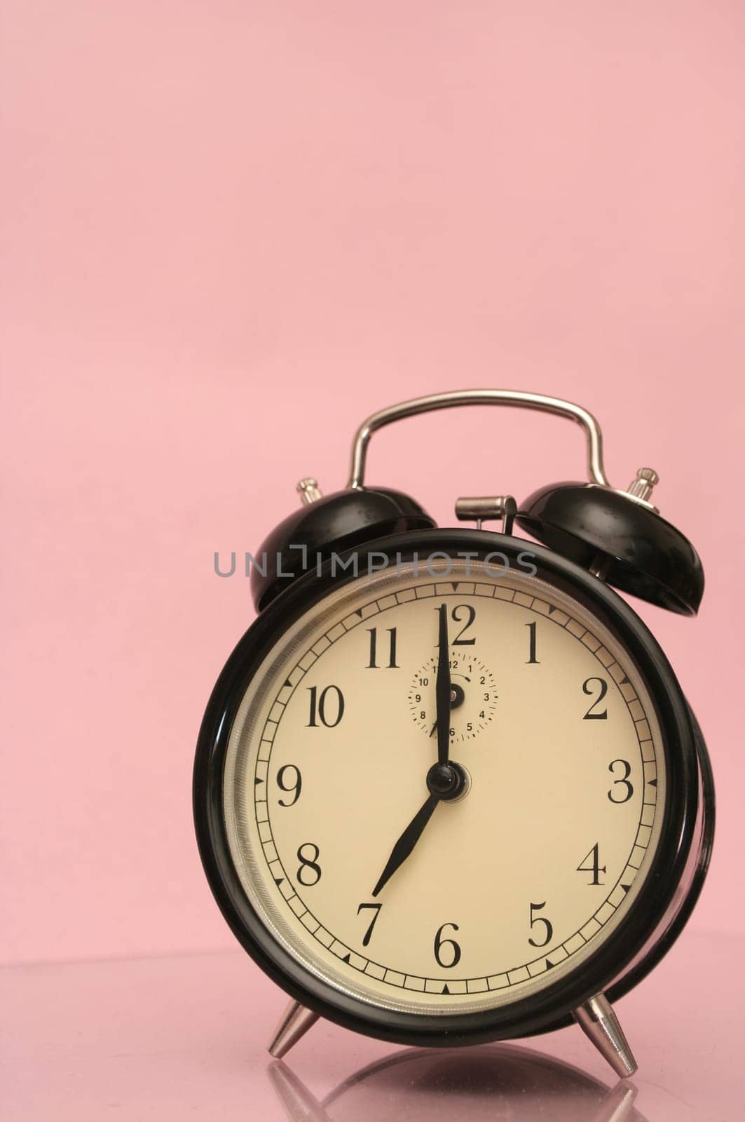 The black alarm clock is on a pink background