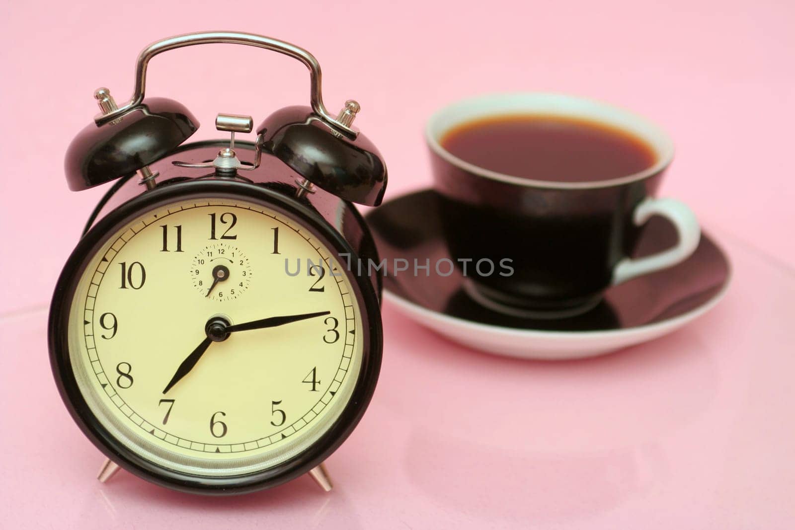 The black alarm clock and black cup from coffee is on a pink background