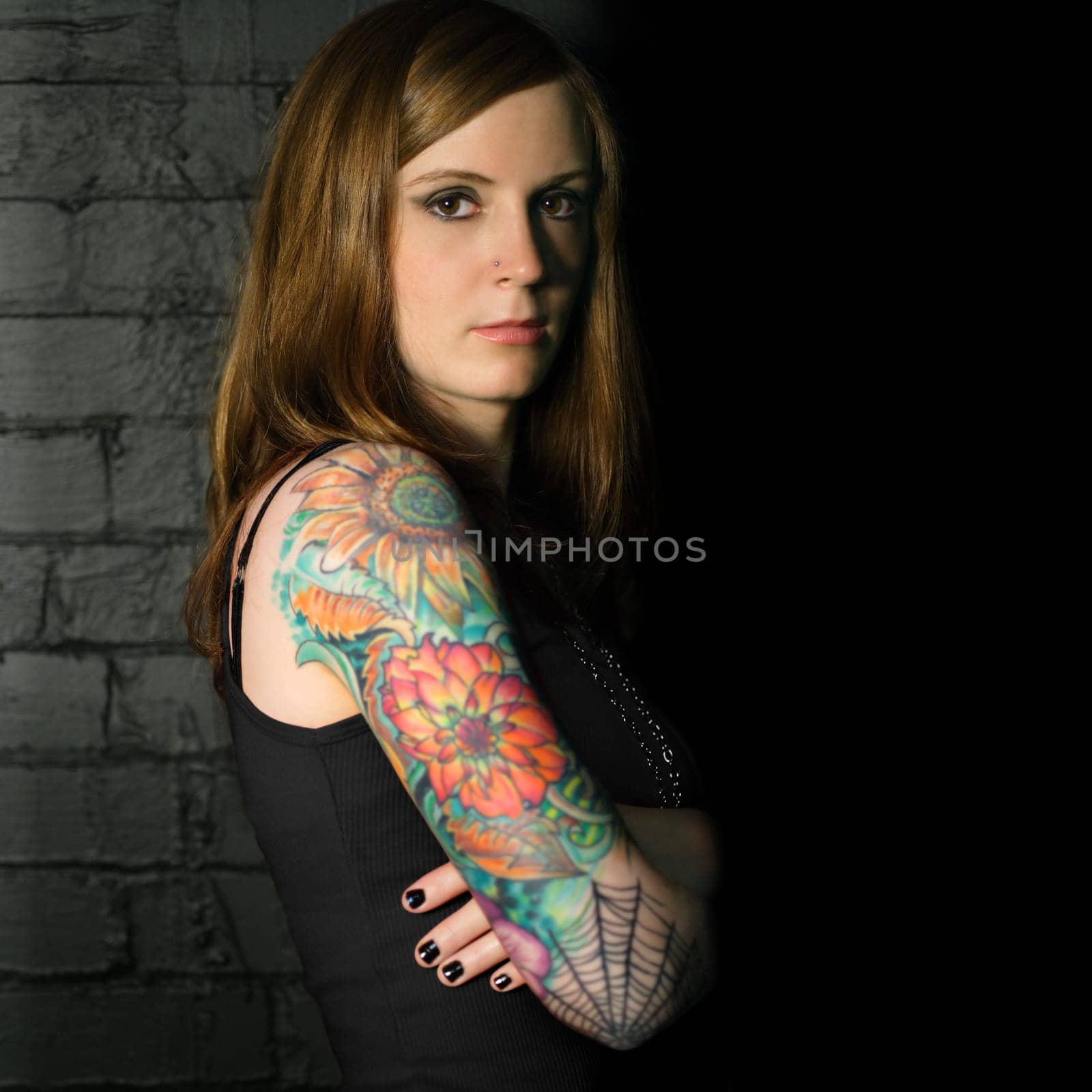 A young female with full arm tattoo leaning up against a black brick wall.