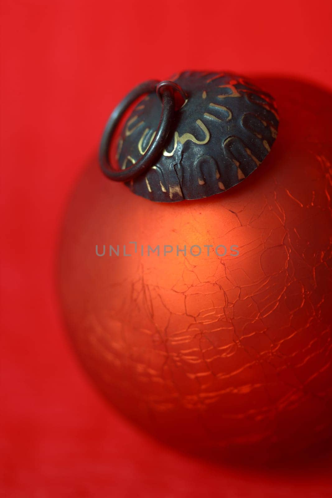 A single red Christmas ball sitting on a red background.  Shallow depth of field - focus on hanger.