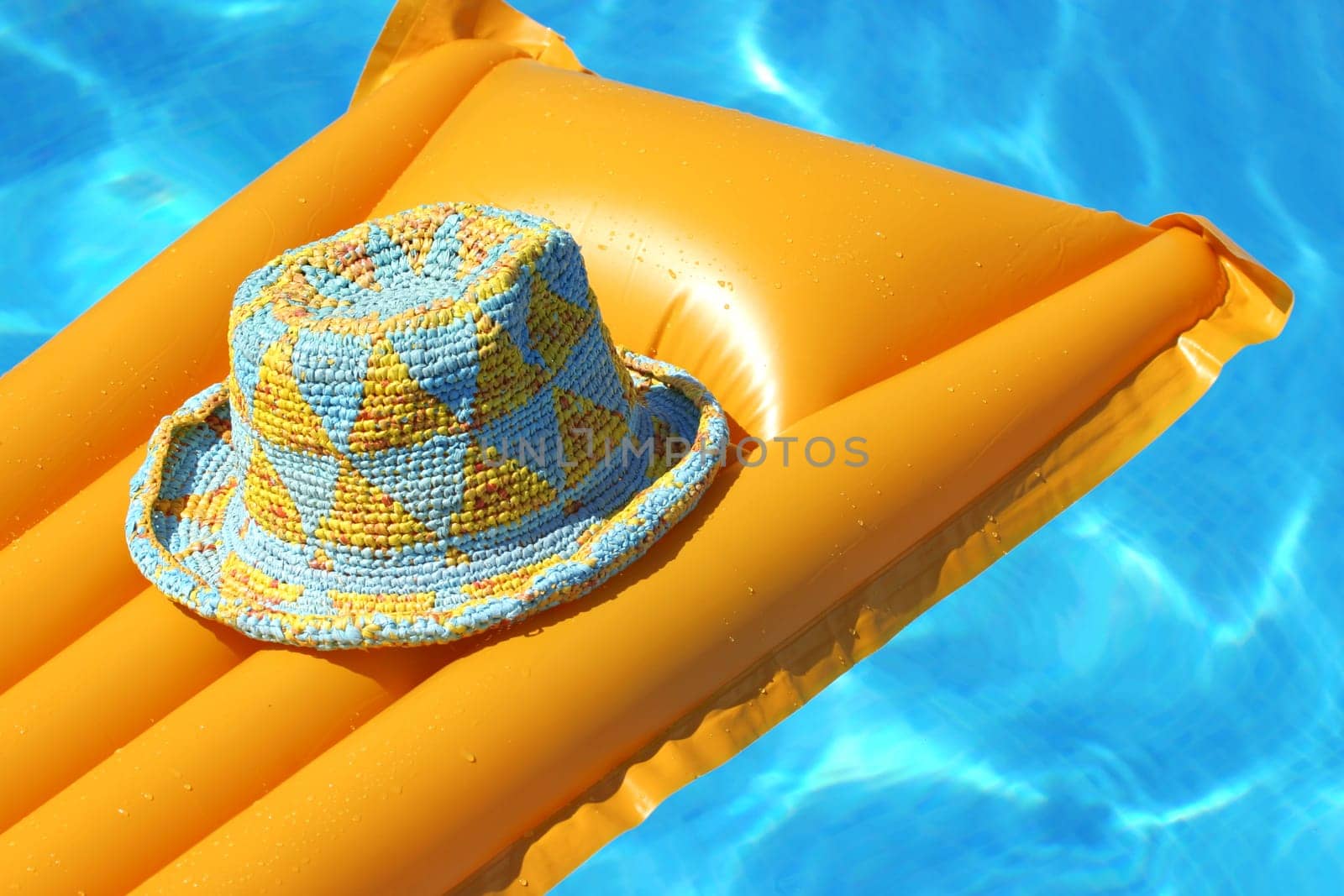 colourful hat on yellow airbed, floating in bright blue water