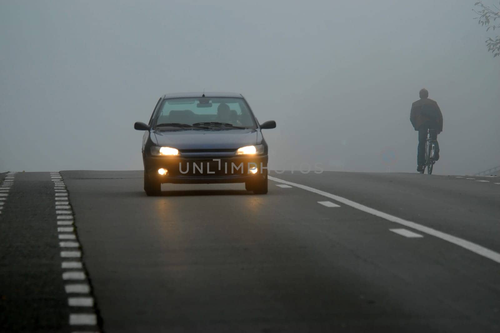 Car appearing through fog with headlights on a cyclist riding into the fog