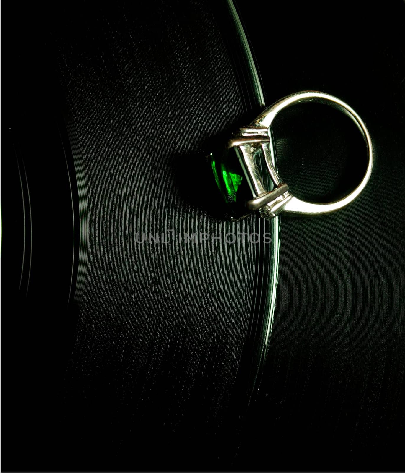 a white gold ring with a green stone lying on a vinyl disc
