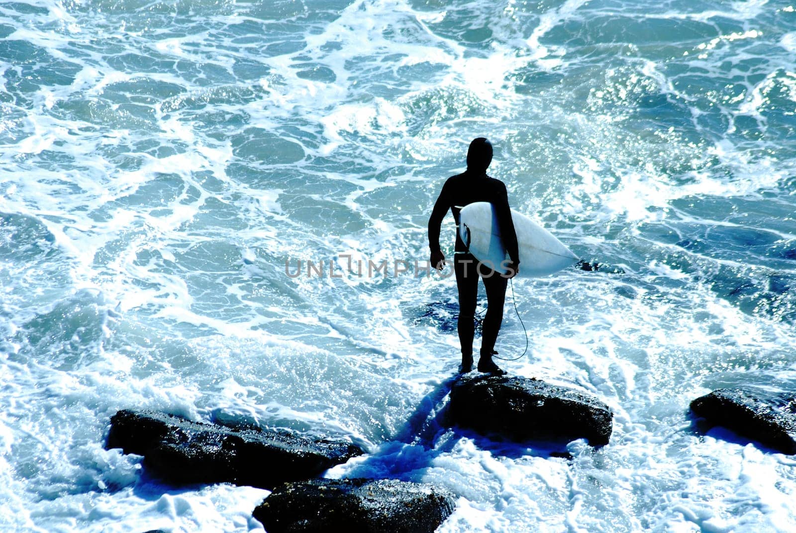 Surfer in wetsuit holds tightly onto his surfboard before jumping into the cold Pacific Ocean in Malibu, California.