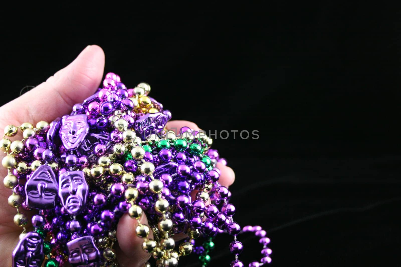 Hand holding Mardi Grass beads with a black background.