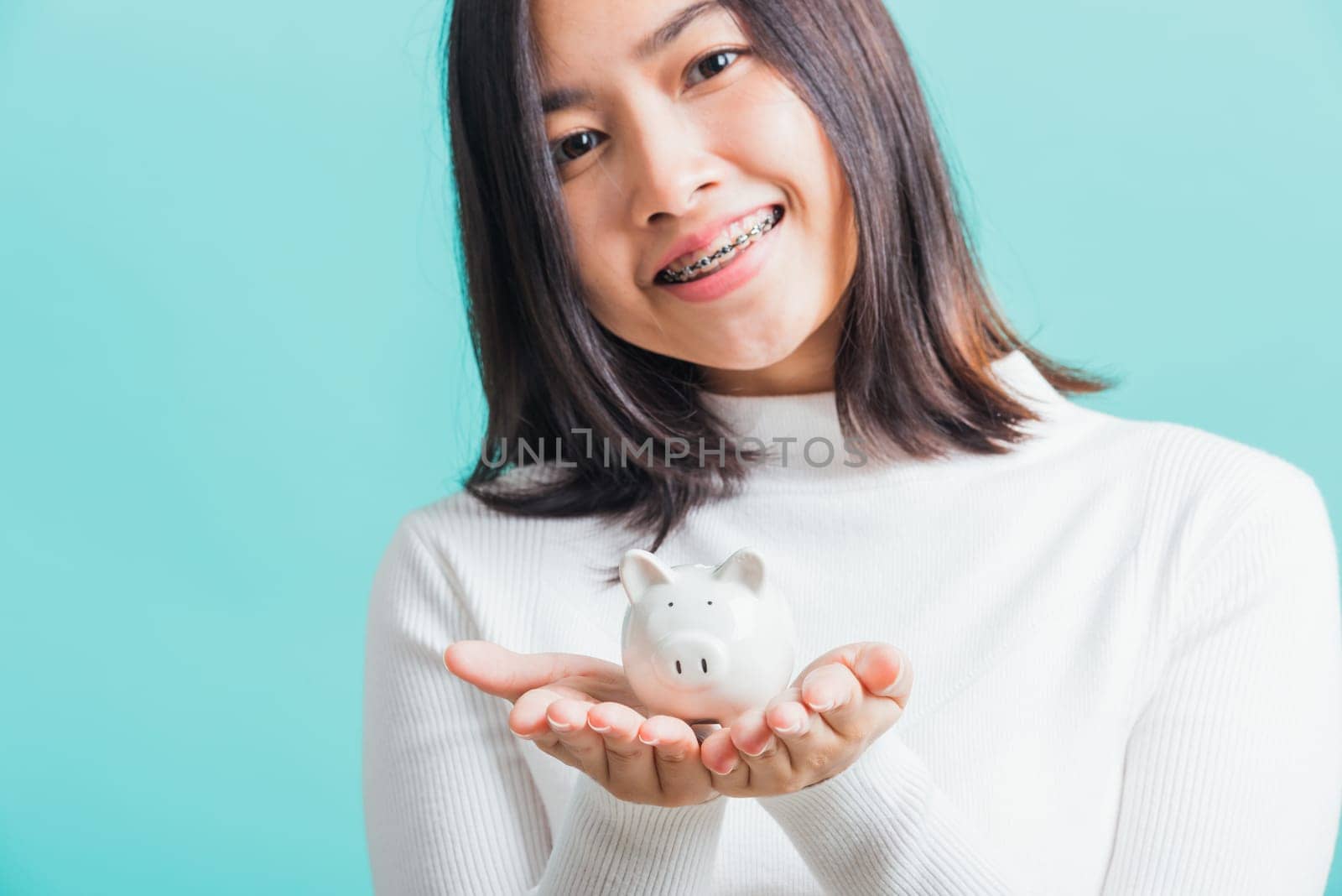 Asian beautiful young woman holding piggy bank on hands, portrait relaxation of happy female smiling hold piggybank in palm, studio shot isolated on blue background, concept of saving money
