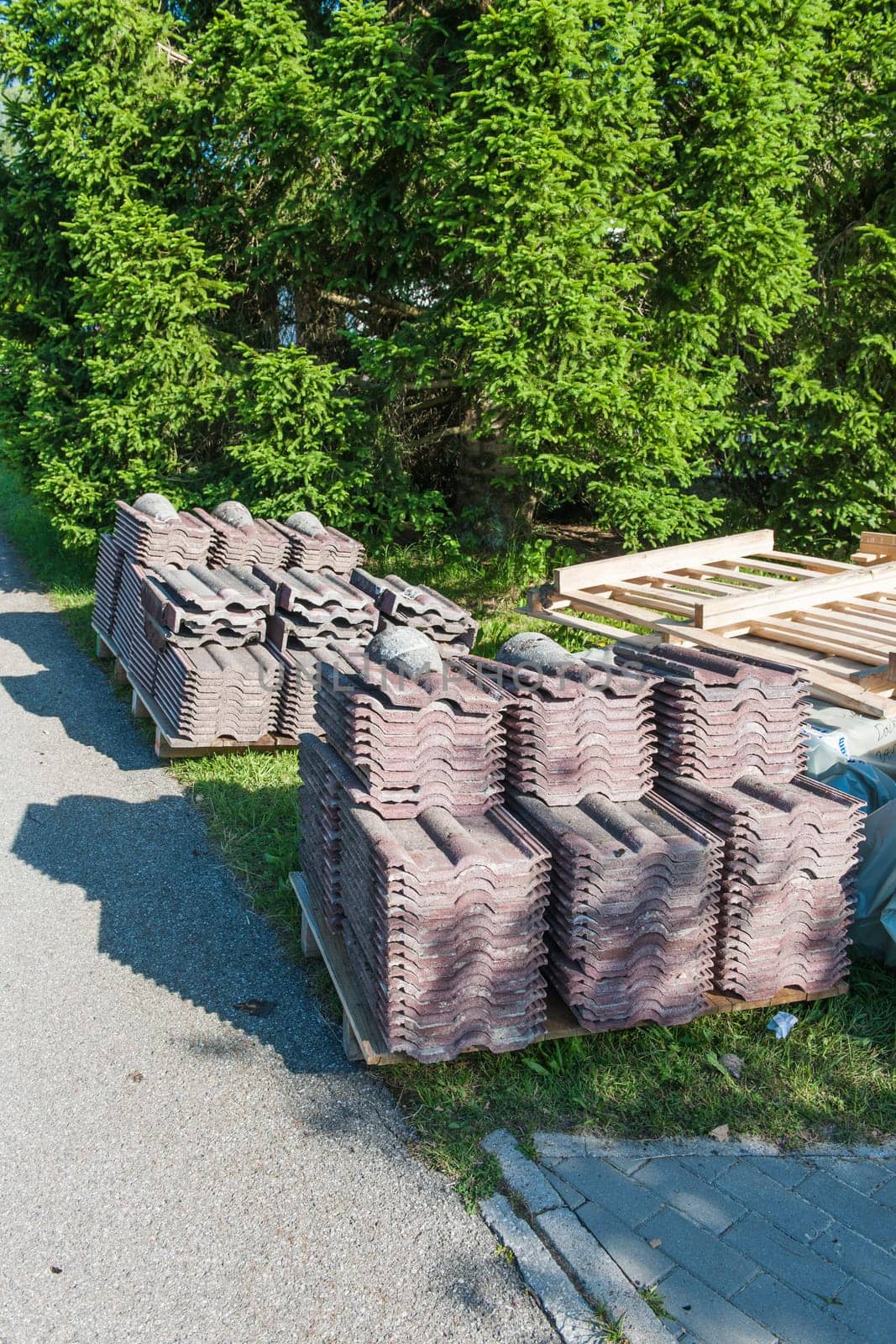 Old dismantled roof shingles after replacement neatly stacked on pallets in sunny side light with shadows.