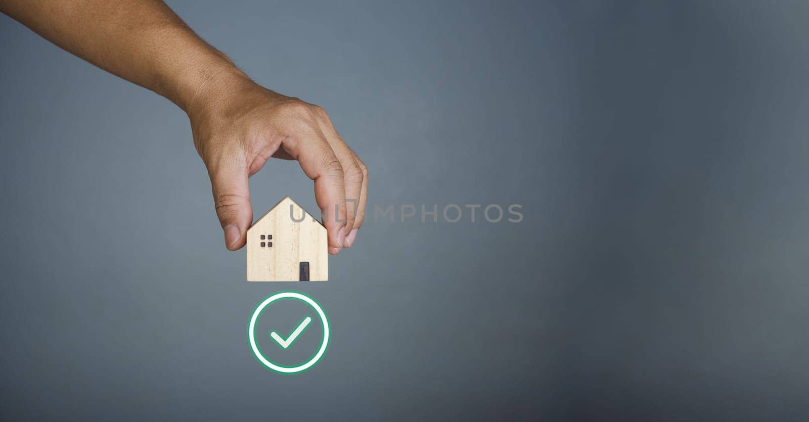 Concept of selling a house. A hand is holding a model house on a gray background. Real estate agent offer house, property insurance and security, affordable housing concepts, home insurance broker agent, salesman person.