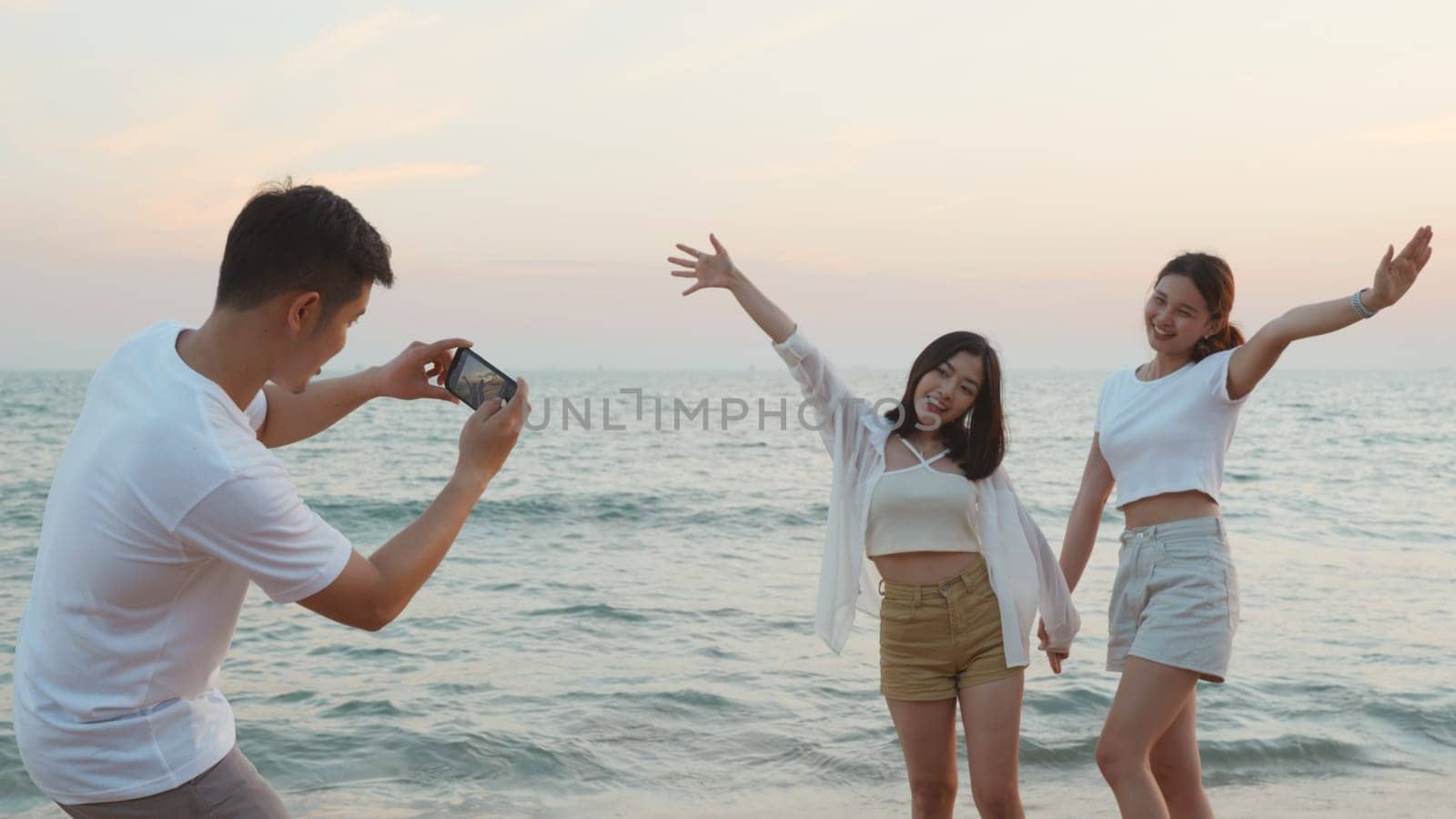 Happy friends smiling and posing taking photo from smartphone and having fun together on beach in holiday vacation time at sunset, Young Asian group woman and man in summer travel outdoor