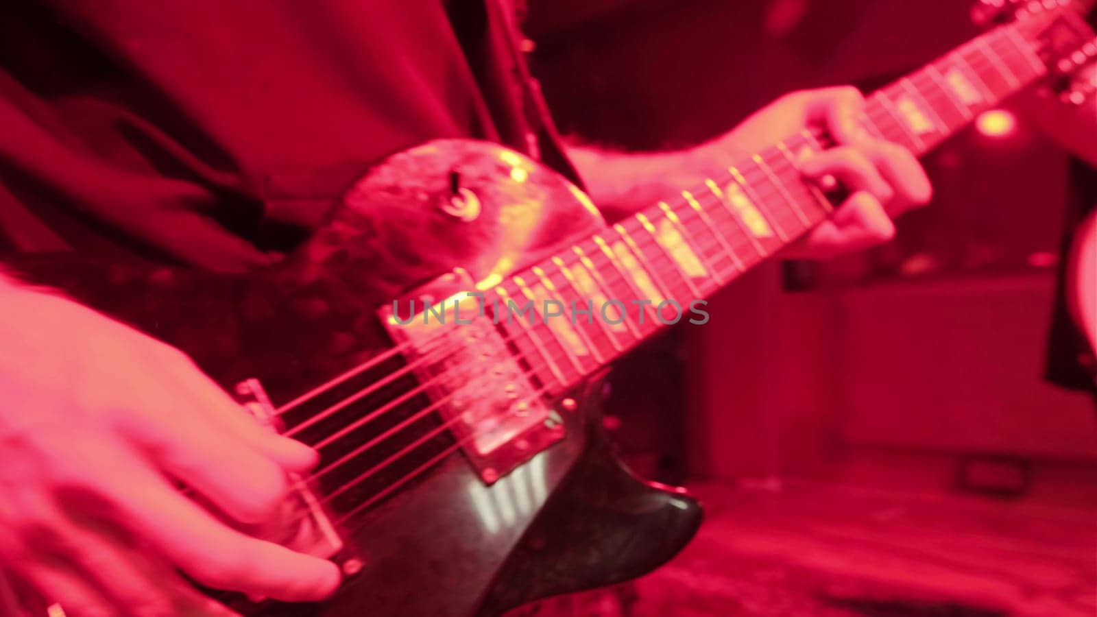 Repetition of rock music band. Cropped image of electric guitar player in a red light.