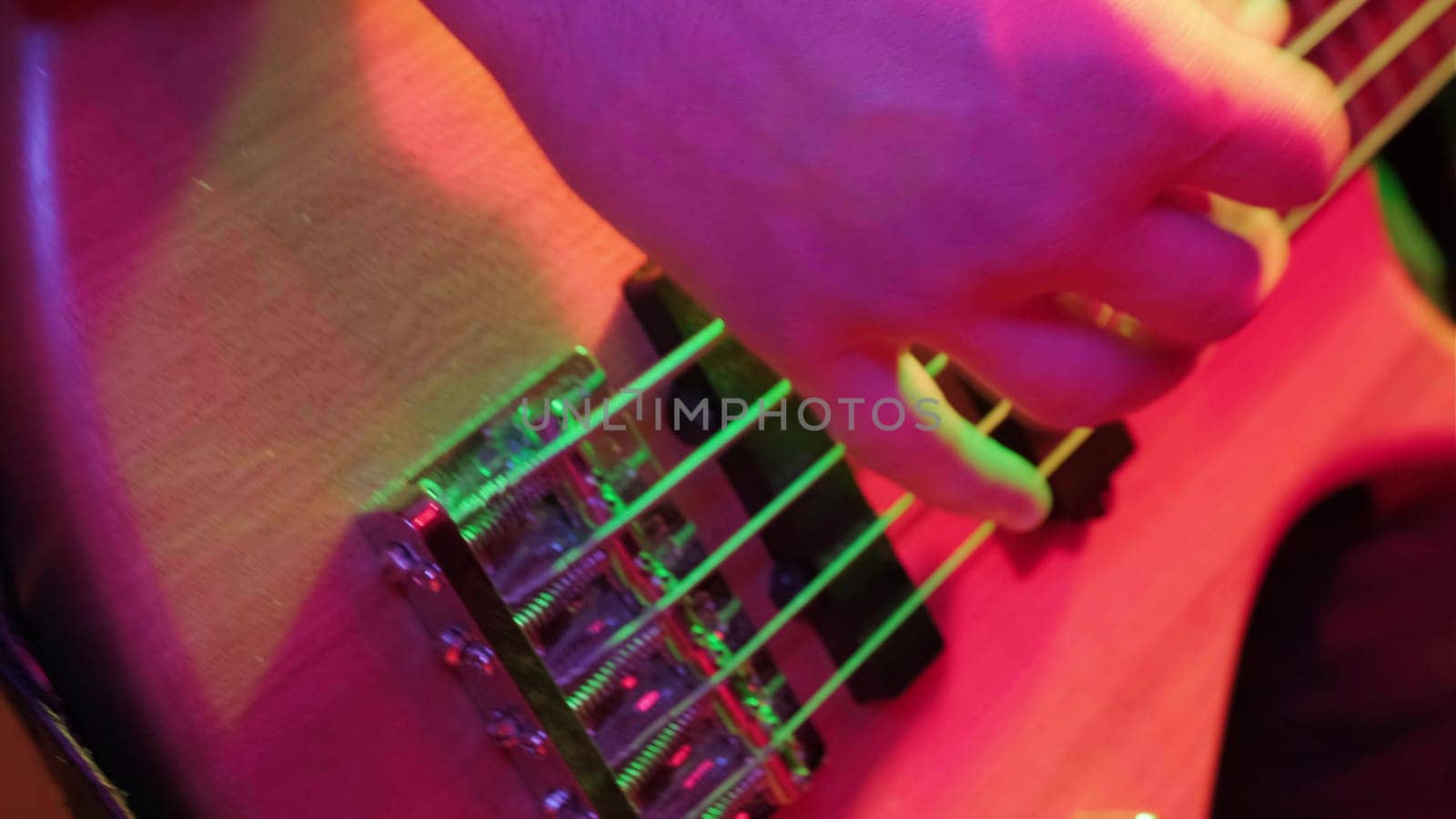 Hands of rock musician playing the electric bass guitar on repetitin in red light.