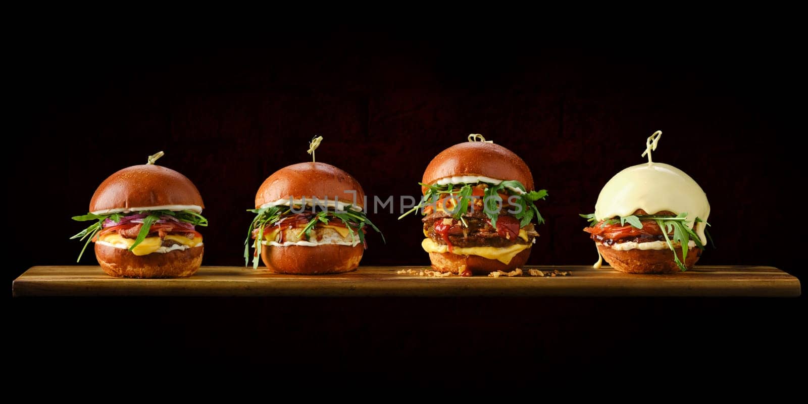 Set of four burgers with different types of meat on wooden serving board