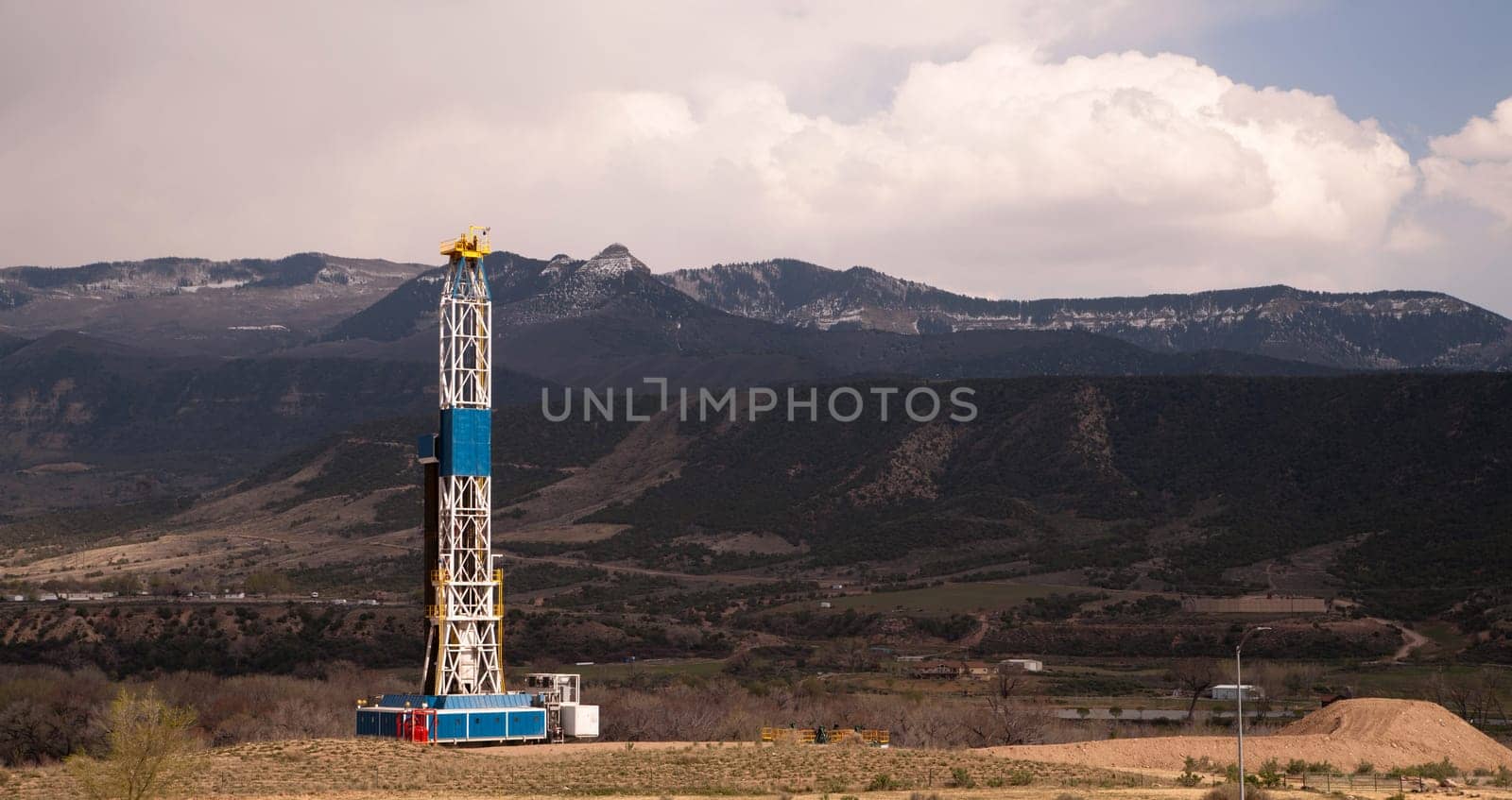 An oil derrick stands late in the day against the mountains
