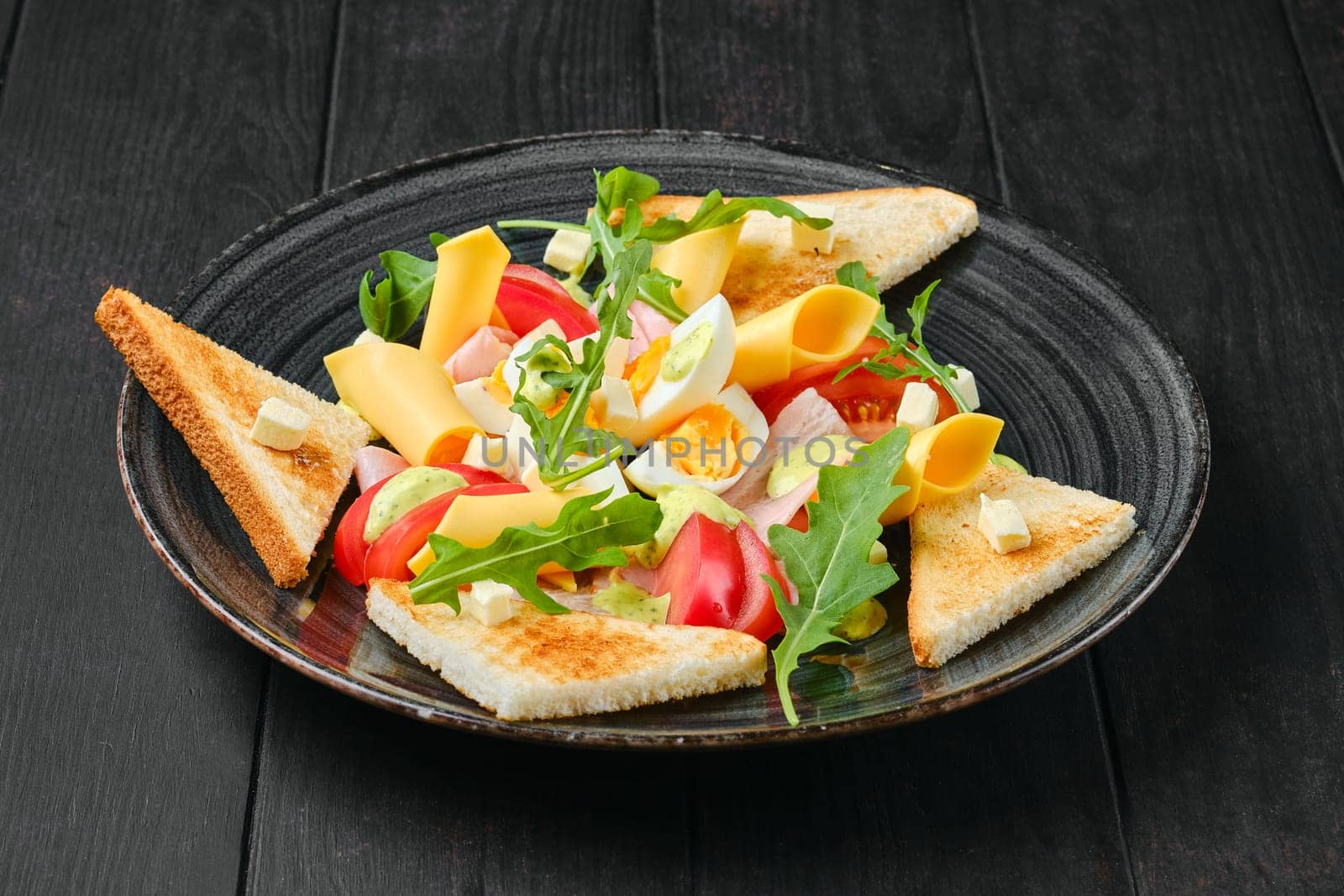 Boiled eggs with slices of toast, cheddar, ham and tomato on black wooden table