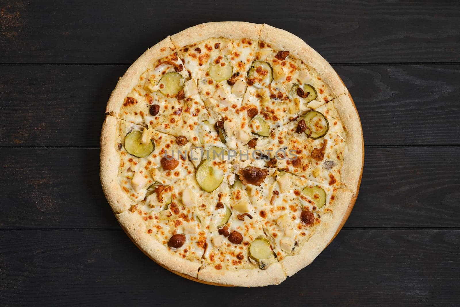 Pizza with chicken, honey mushrooms and pickled cucumber on dark wooden table