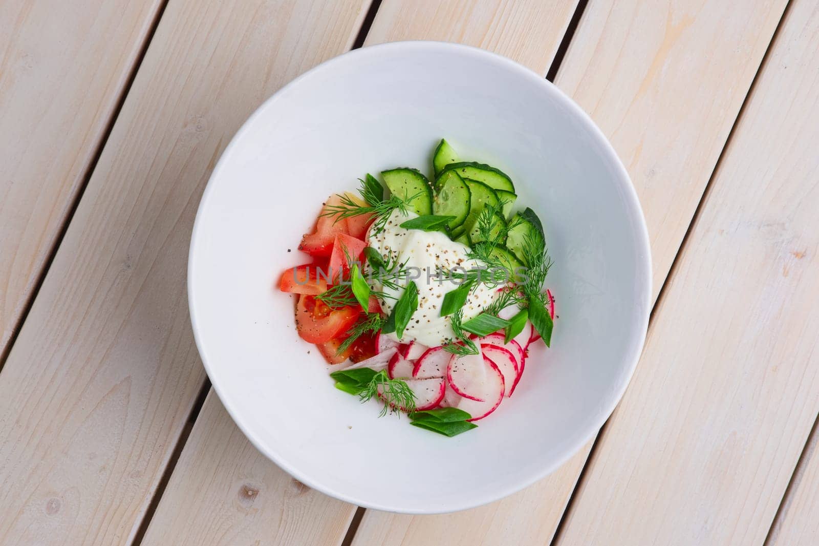 Top view of salad with radish, tomato, cucumber, onion and sour cream