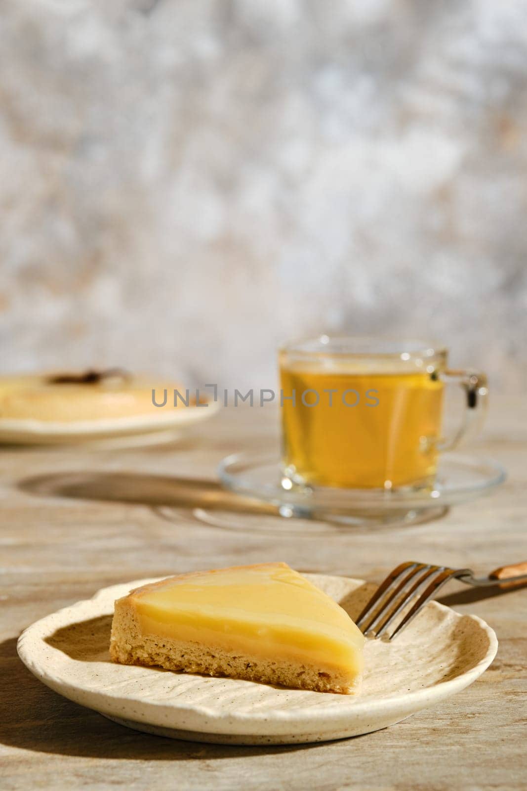 Piece of lemon tart with tea under direct sunlight with hard shadows on the table
