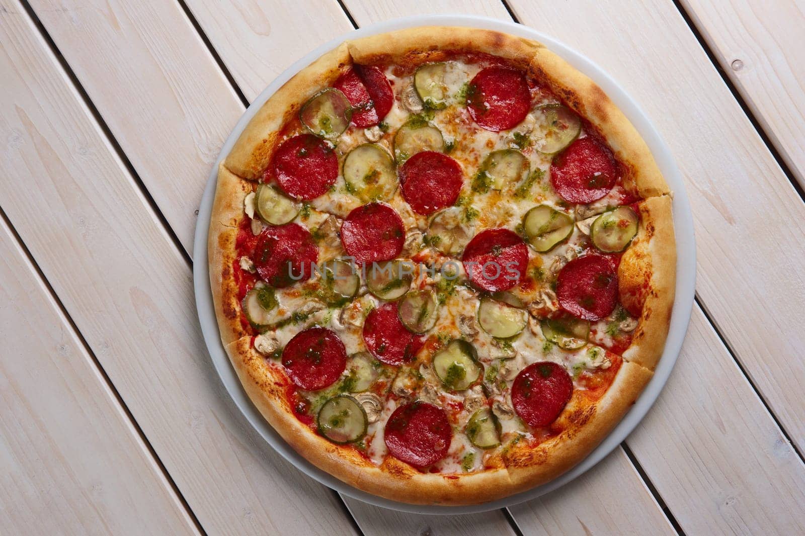 Top view of whole pizza with sausage, pickled cucumber and mushrooms