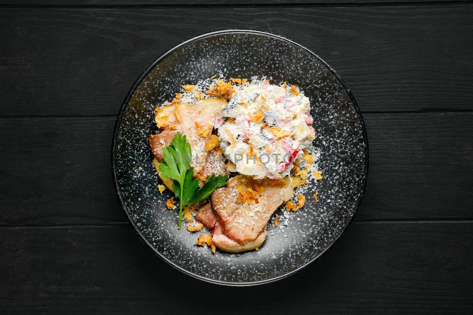 Overhead view of fried ham with salad sprinkled with bacon chips and grated parmesan on a plate