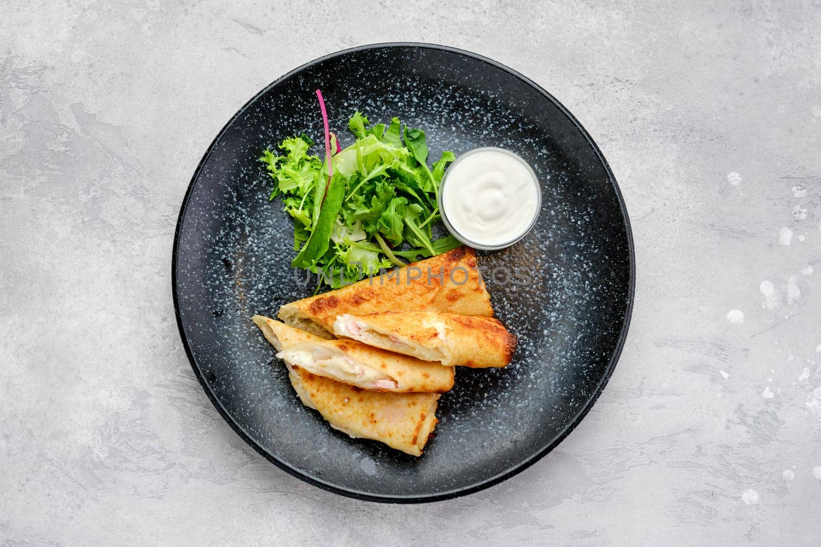 Top view of thin crepe stuffed with melted cheese and ham on a plate