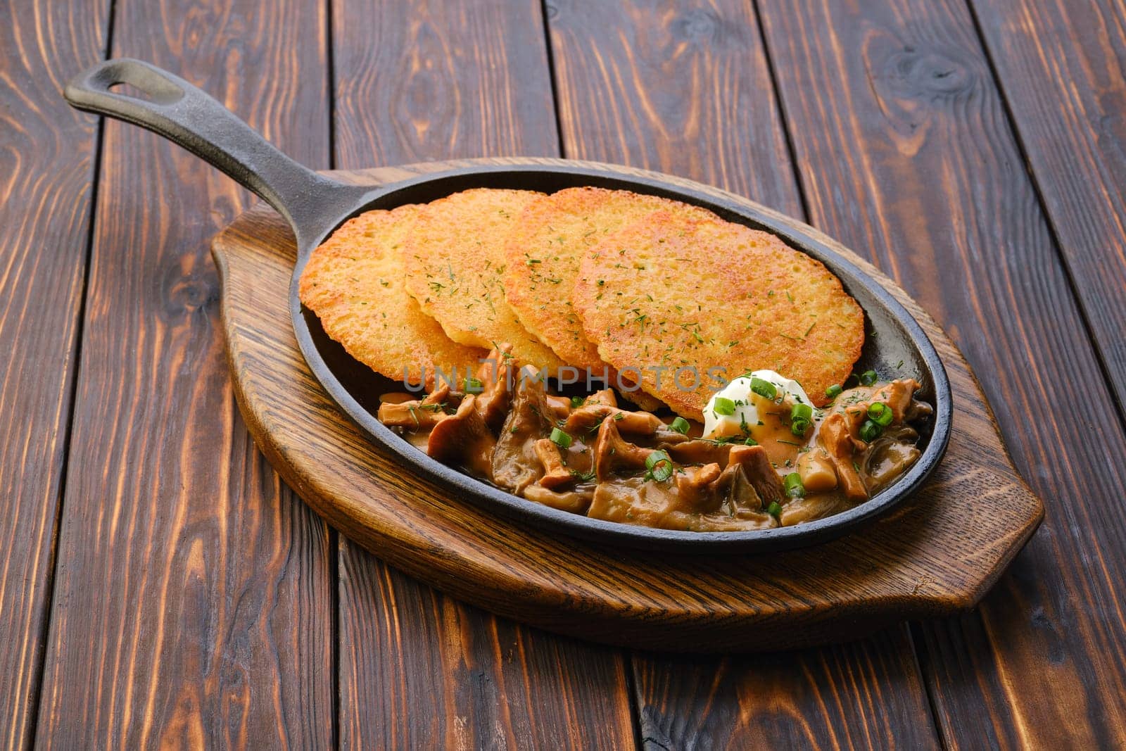 Cast iron skillet with fried chanterelles, honey mushrooms and potato pancakes with creamy sauce