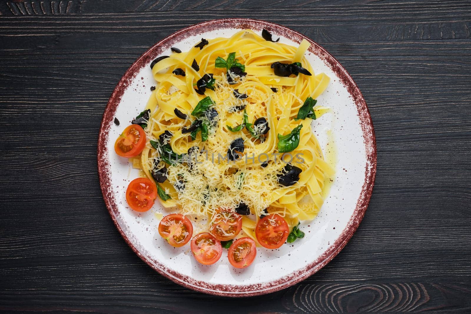 Top view of tagliatelle with tomato, parmesan, chopped olives and basil